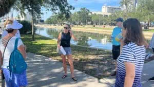 Monica Kile explains the history of Demens Landing on the St. Pete Waterfront with Al Lang Stadium's parking lot behind her