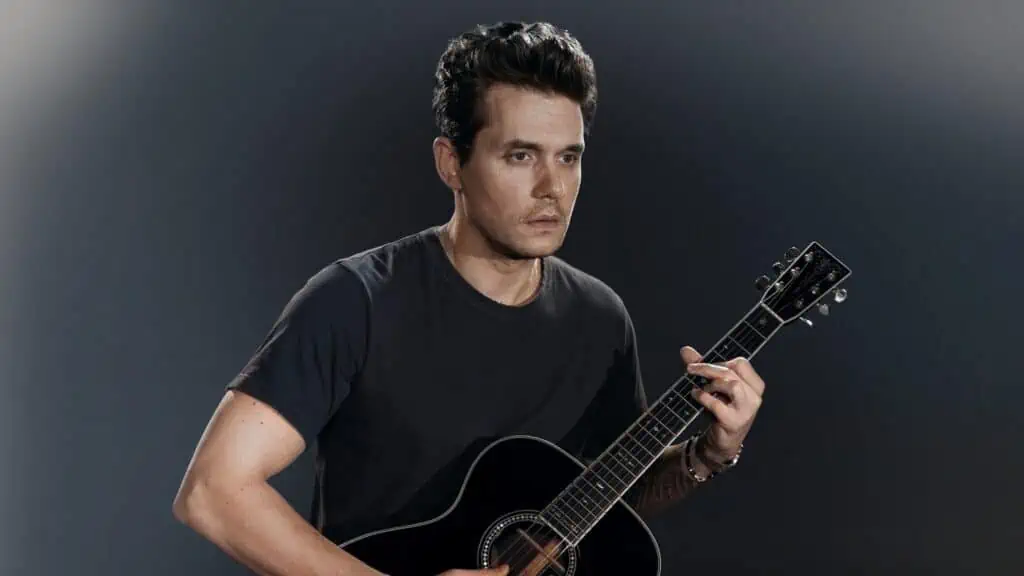 John Mayer holds a guitar and stares into the distance