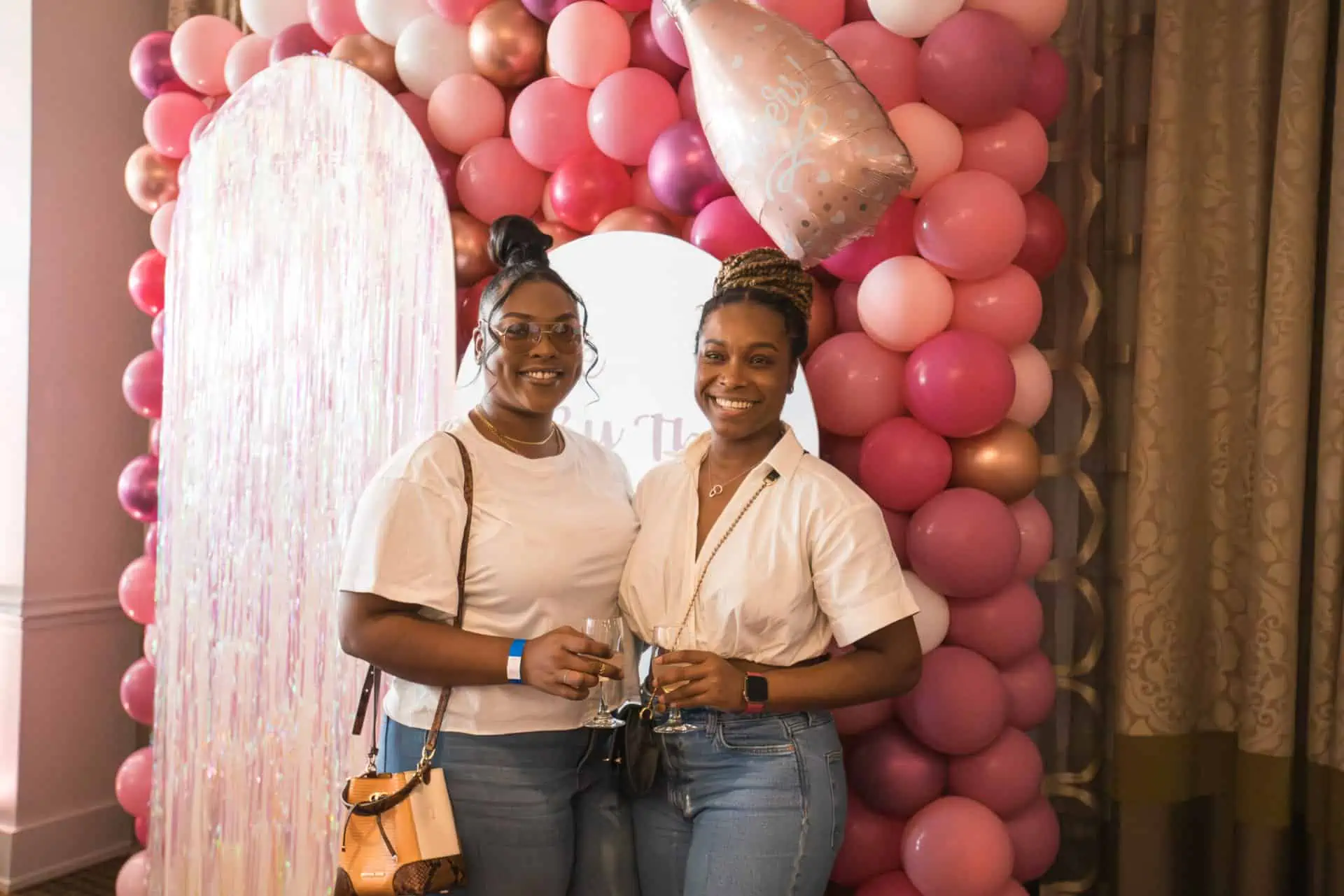 two women stand in front of a pink and white balloon arrangement