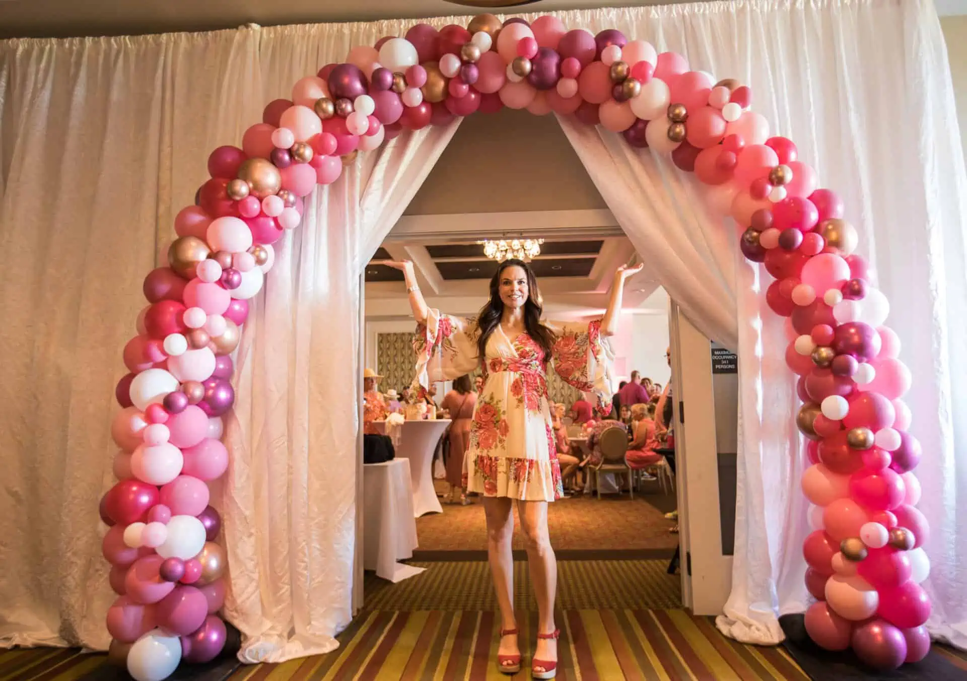 A woman stands below a pink balloon arch