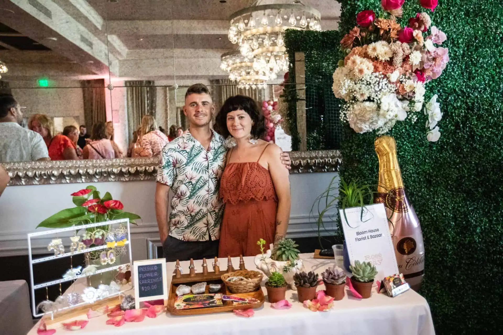 the owners of bloom house and florist bazaar smile while standing behind their table