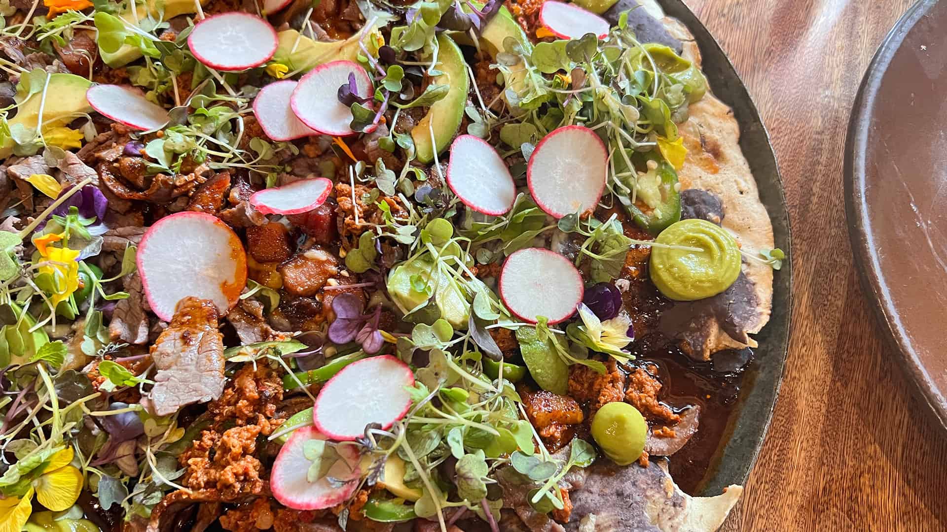 Close up of the Tlyuda Cecina. A plate of corn tortilla covered in guacamole, chorizo, cecina, black beans and spices