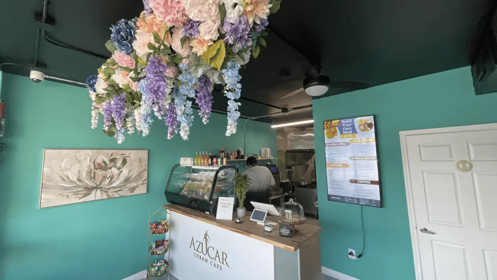inside a cafe with blue walls, a pastry case, and flowers over the counter