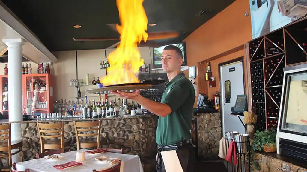 a waiter with a plate set ablaze for show inside a restaurant 