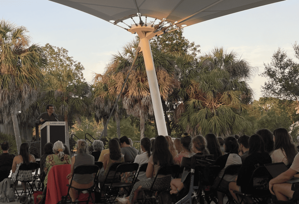 people attend an outdoor poetry reading on a waterfront campus