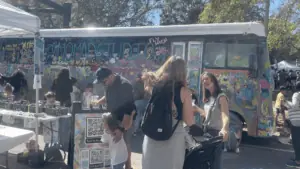 people gather around a mural covered bus at an outdoor festival