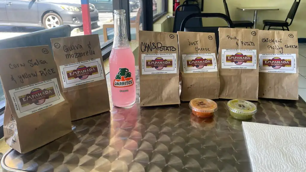 six bags with empanada flavors written on them sit on a table with a guava Jarritos soda