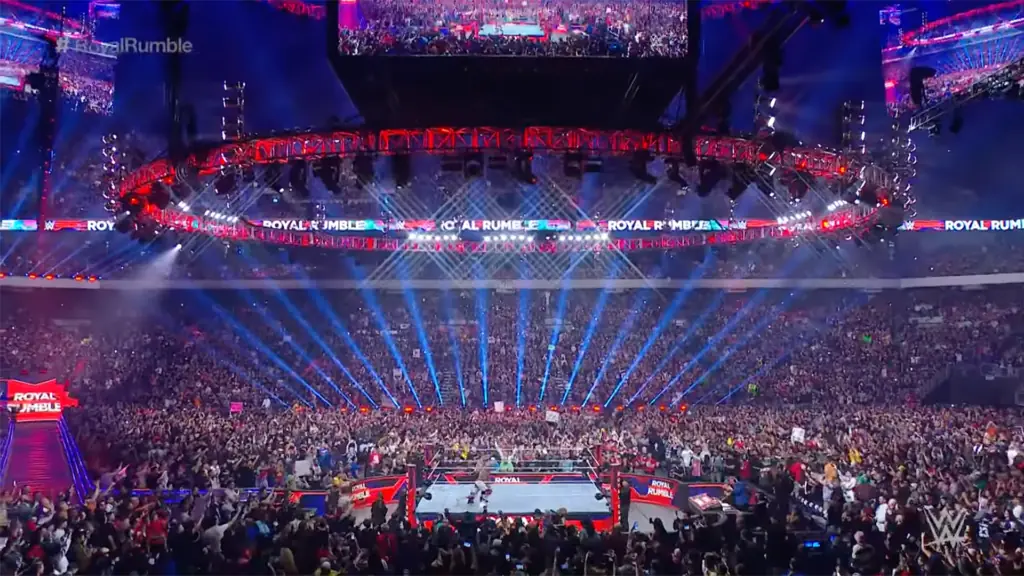 a wrestling ring surrounded by lights in a sold out stadium