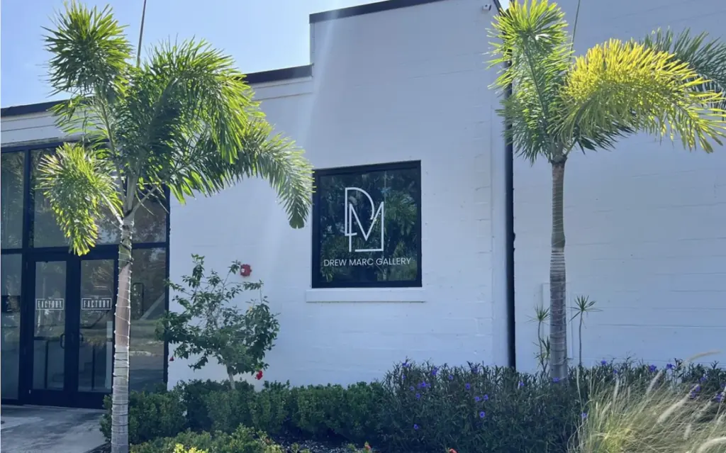 exterior of white building with palm trees and the words "Drew Marc Gallery" on the window