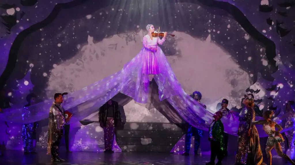 a performer on stage playing violin while performers dance beneath her