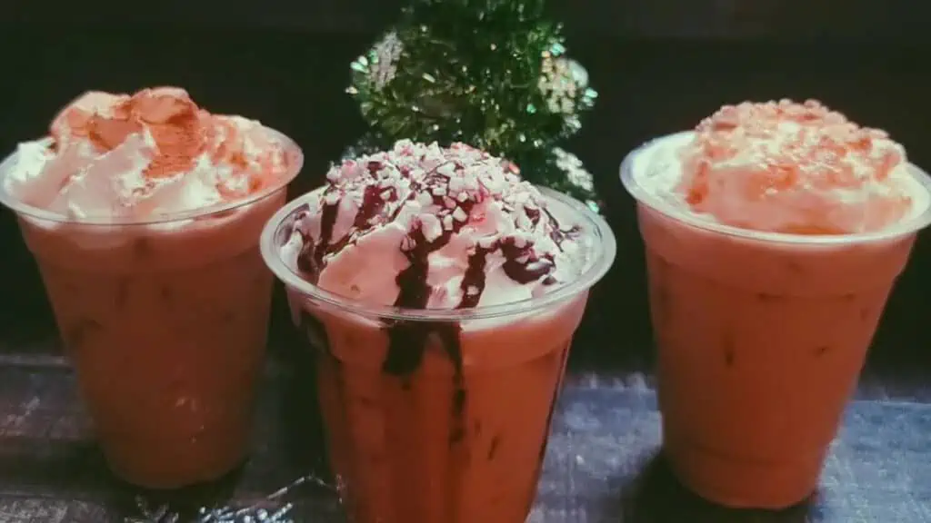 three holiday lattes topped with whipped cream in a window sill