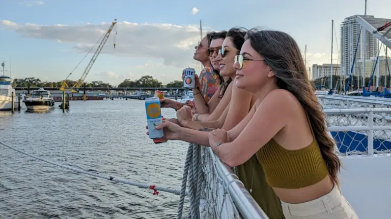 Four young women holding cans looking over the bow of a ship into the distance