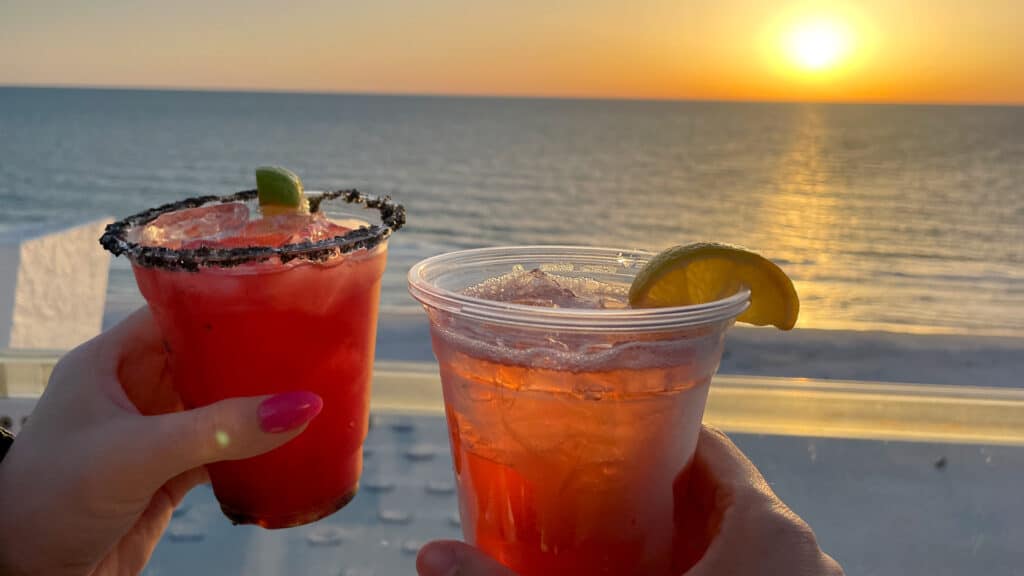 two colorful cocktails in front of the sunset on a rooftop beach bar