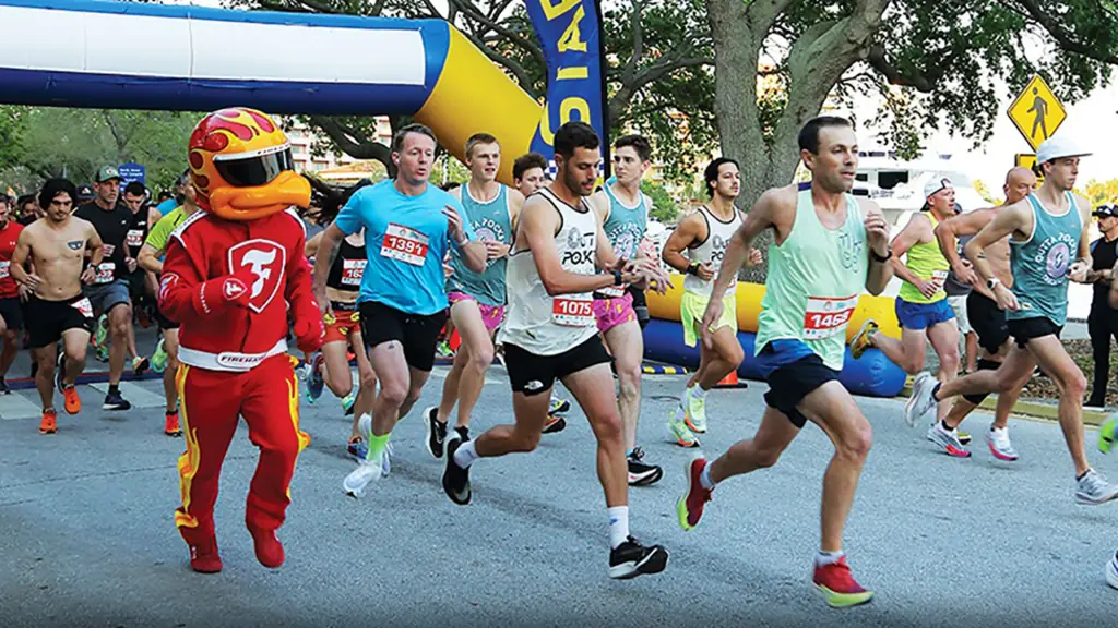 a group of runners participate in a community 5K. A red bird mascot is running alongside the participants