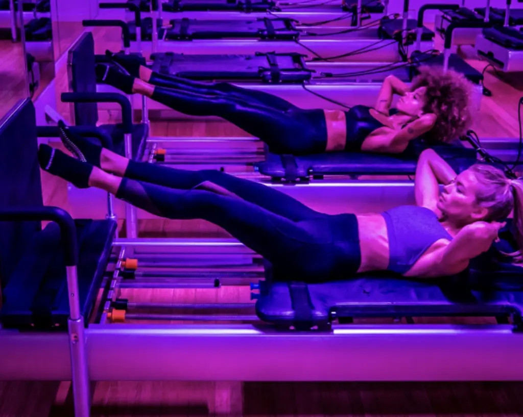 Two women participating in BodyRok style pilates with purple lighting.