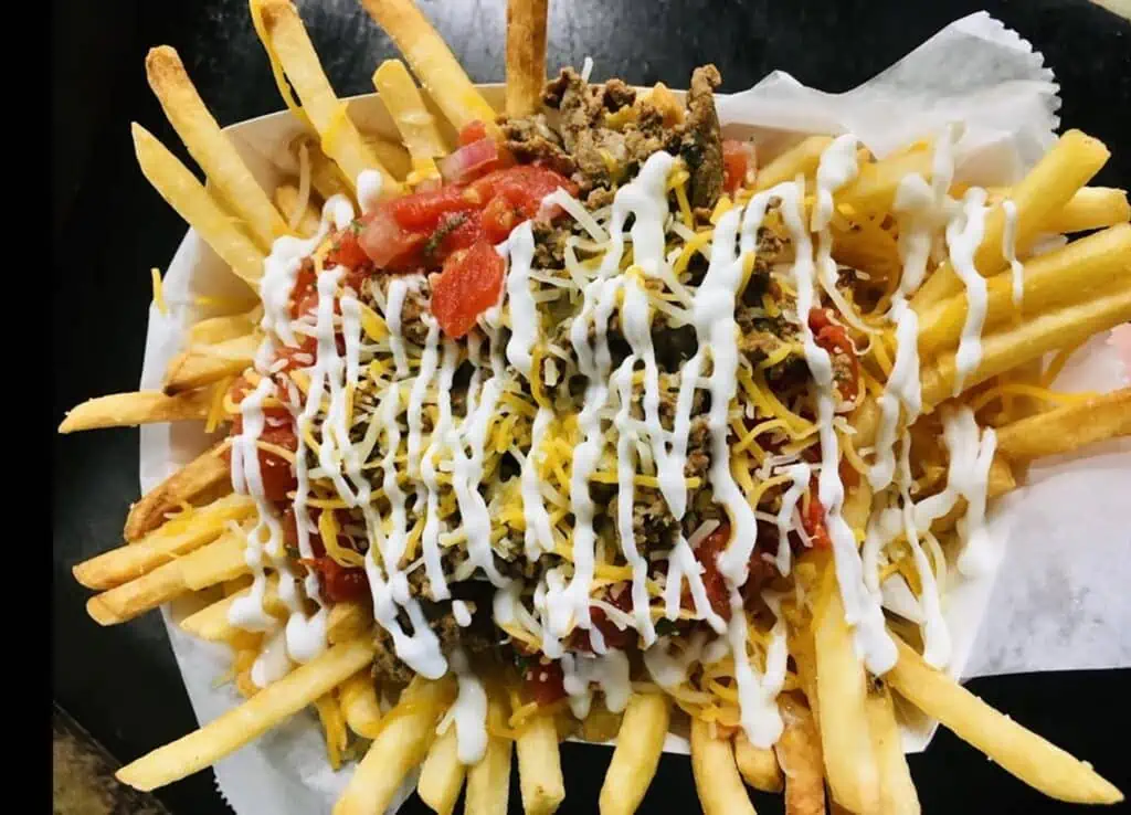 a plate of loaded French fries topped with shredded beef, veggies and cheese
