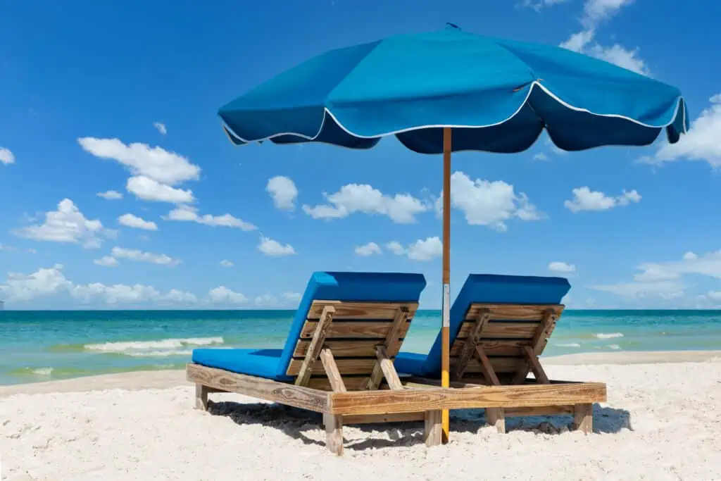 Two beach lounge chairs with a view of the gulf and blue umbrella.