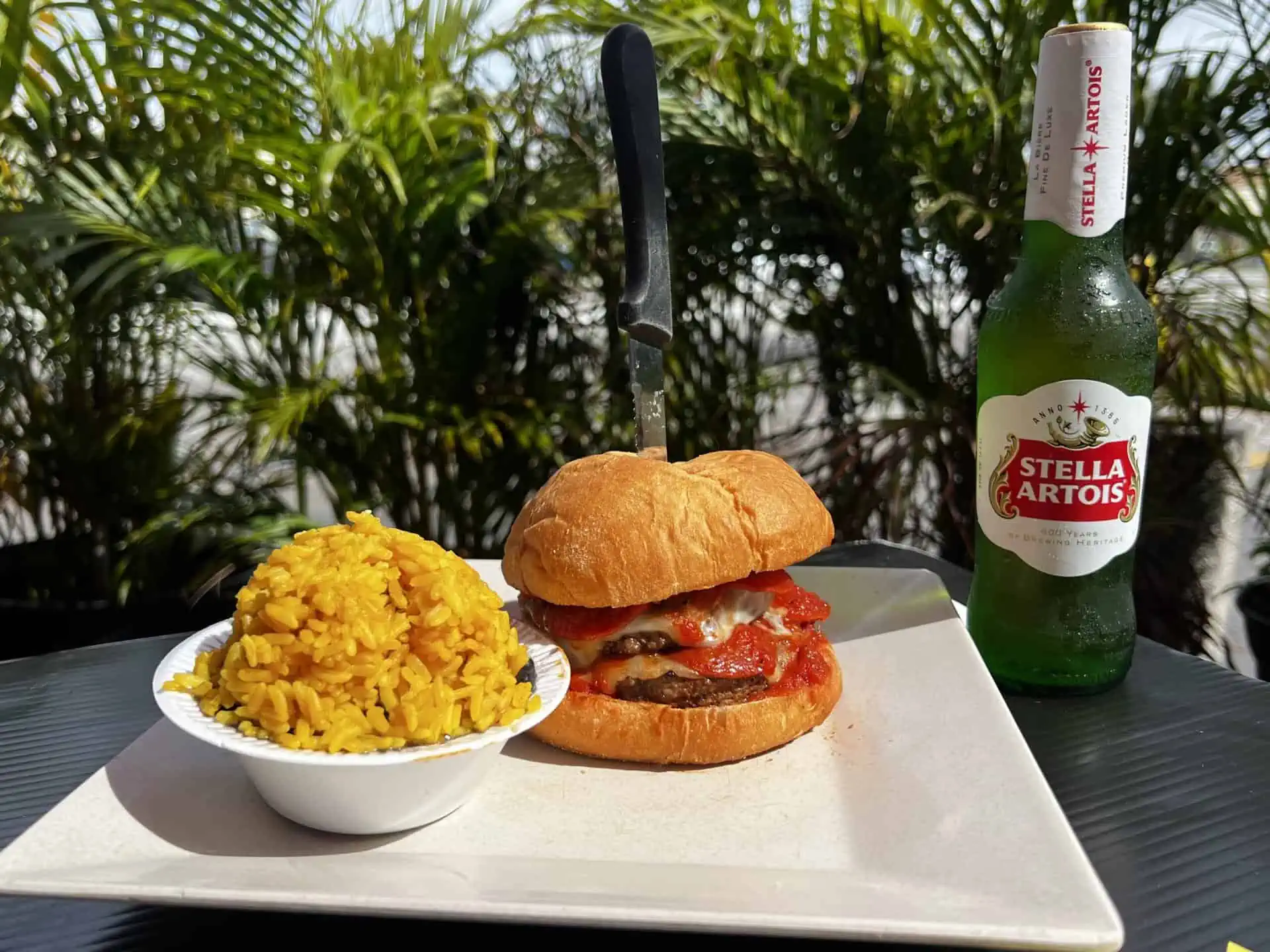 Burger of the Month: Pizza Burger | A burger on a plate with a side of yellow rice next to a bottle of beer