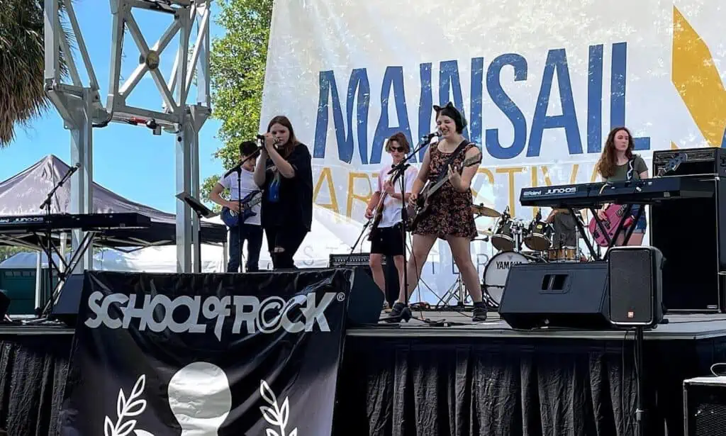 a group of young kids perform live on stage at an outdoor festival. 