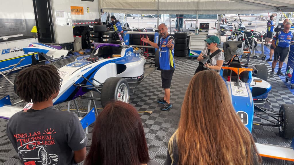 a mechanic explains the different details on an INDYCAR to a group of students