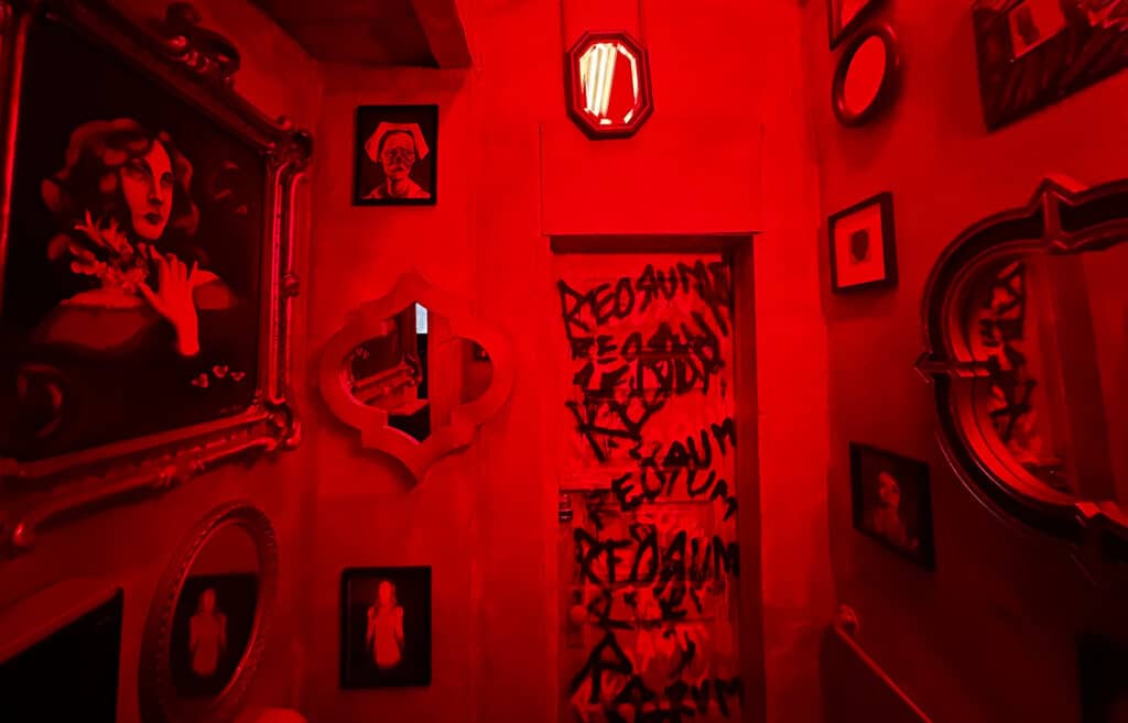 a bathroom with red lights turned on. Paintings are hung on both walls