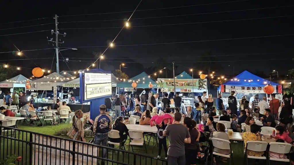 a large food vendor market at night with picnic tables set up and arranged