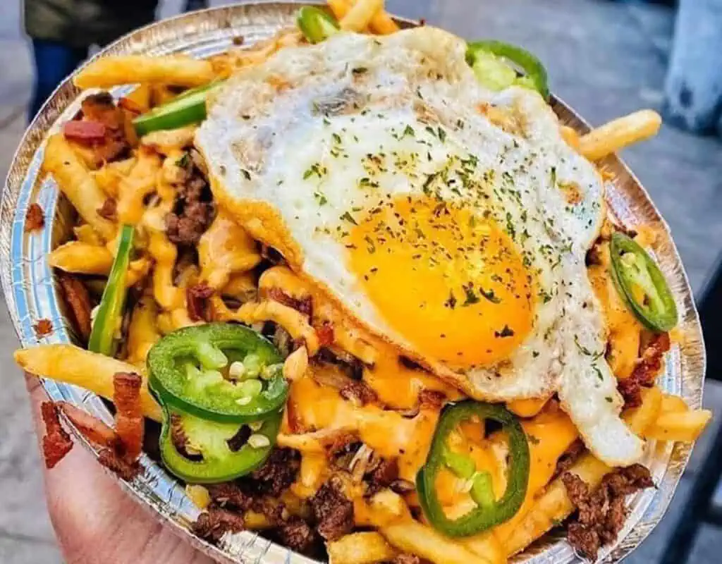 a plate of fries topped with a fried egg and peppers