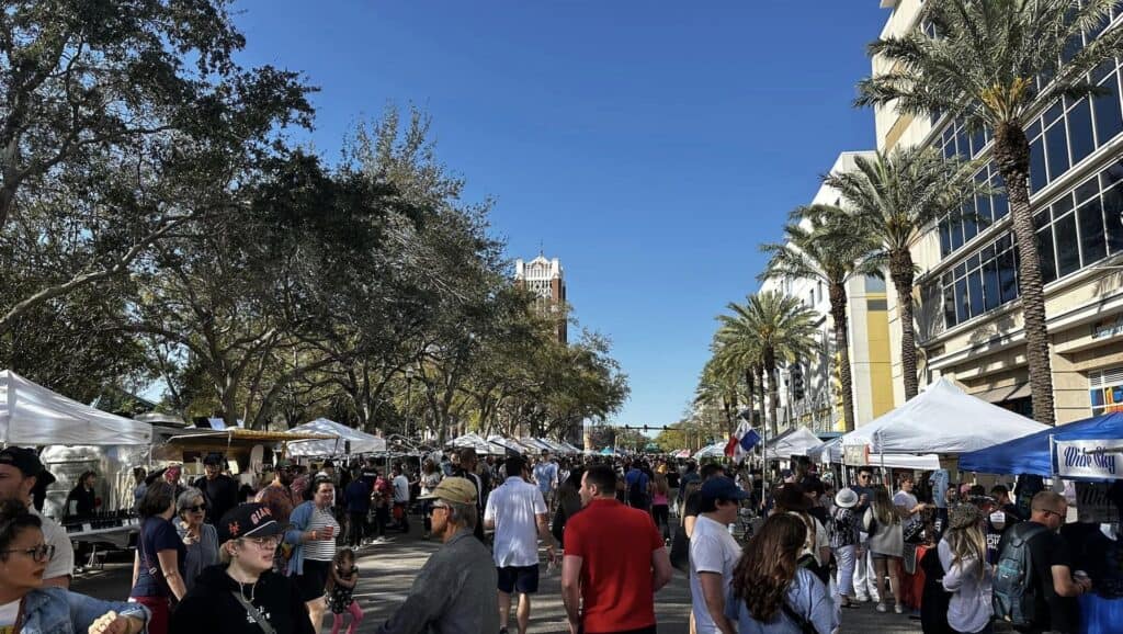 a crowd of people shop at an open air street market in a downtown area