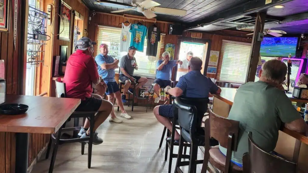 7 Patrons at a bar with most looking at one in particular as he tells a funny story