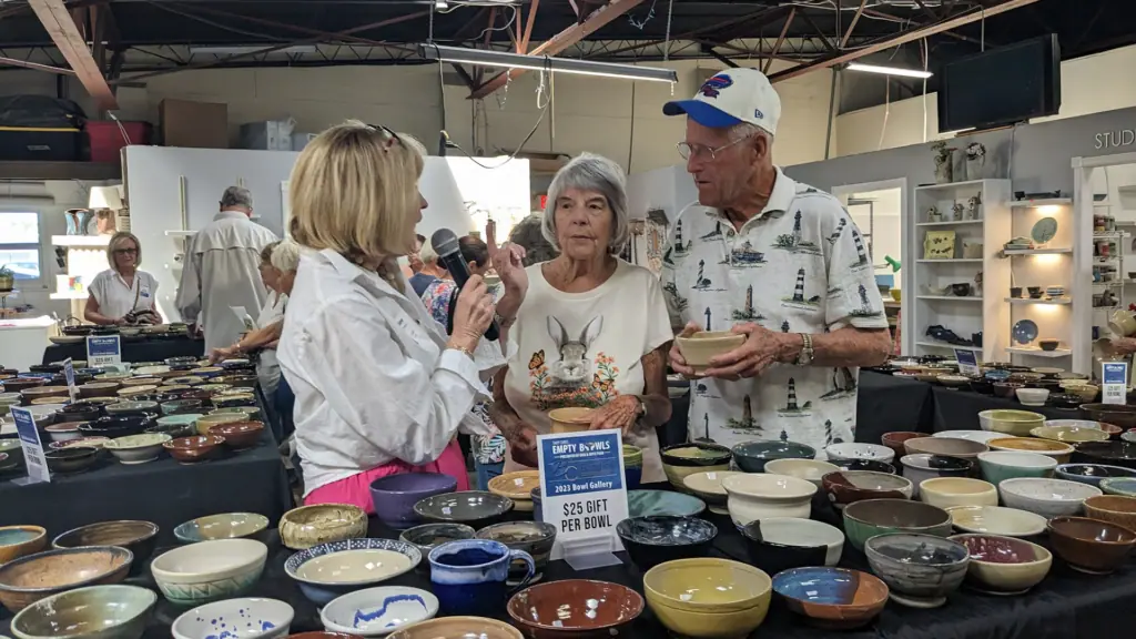a group of people gather around multiple hand made clay bowls at a fundraiser 