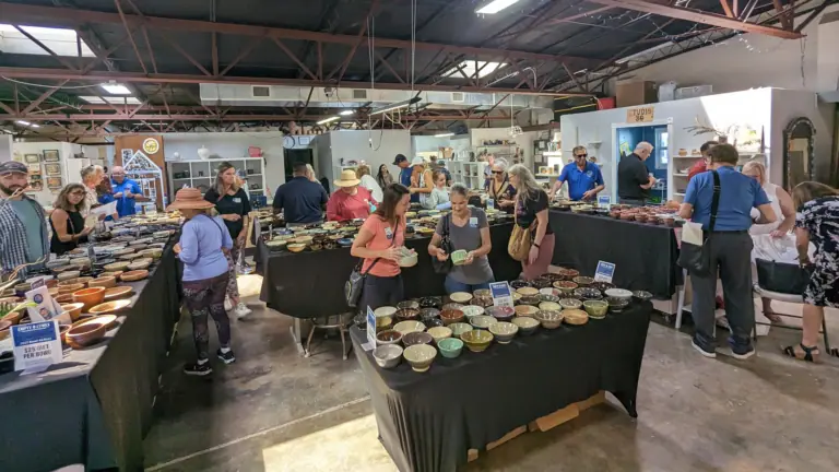 a group of people walk between multiple tables with handmade clay pottery at a fundraiser