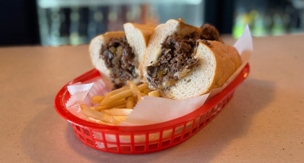 a cheesesteak sandwich on a red platter with fries 