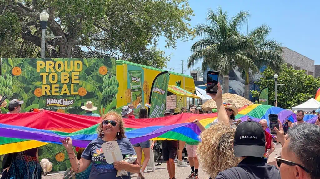 people carry a long rainbow flag down a street 