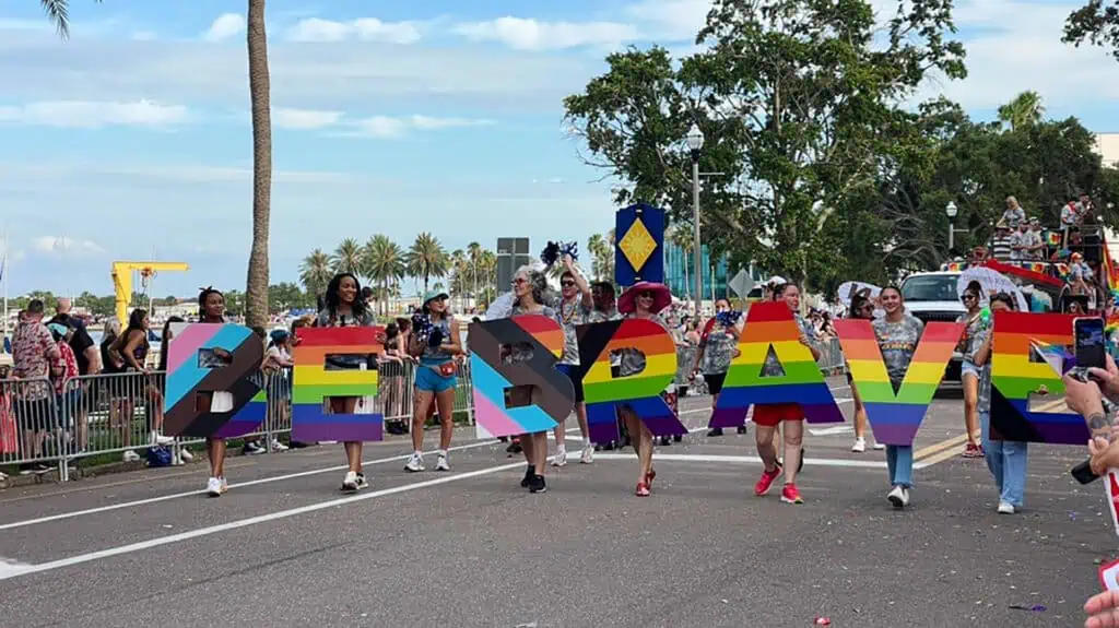 parade participants hold a multi color sign that reads be brave