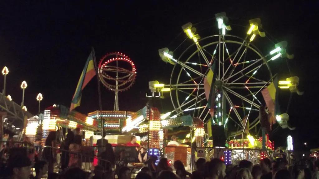 carnival rides lit up at night as visitors travel through lines and toward vendor tents