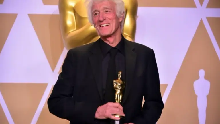 a man in a black suit poses on stage with a trophy.