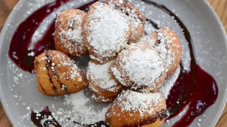 plate of beignets covered in powdered sugar and chocolate sauce