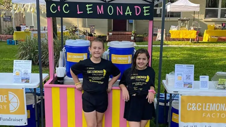 two girls standing at lemonade stand