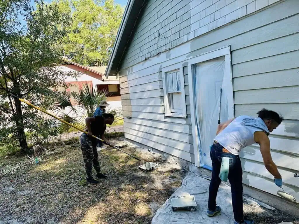 Three CONA volunteers pain a green house white.
