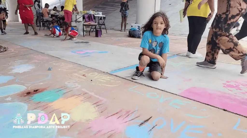 A id poses in front of a chalk art at an outdoor festival