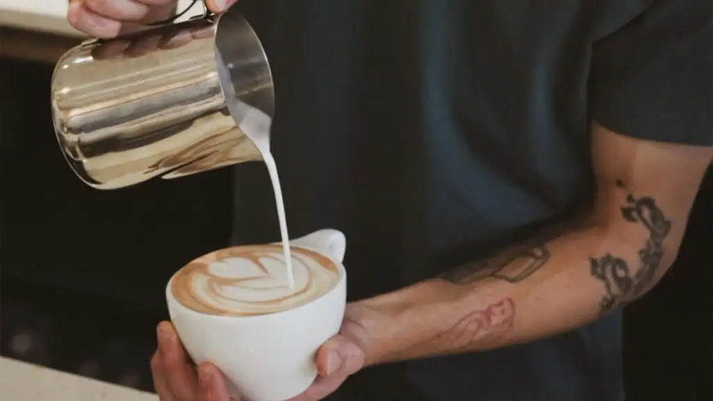a person pours milk over a latte 