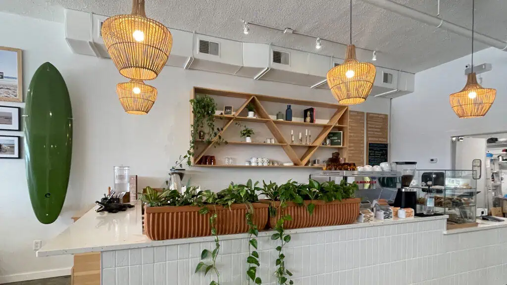interior of a coffee bar with Edison bulbs covered in bamboo hanging over the white tile counter