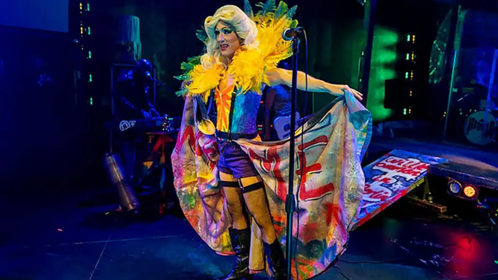 a performer on stage in a blue and yellow dress and a big wig