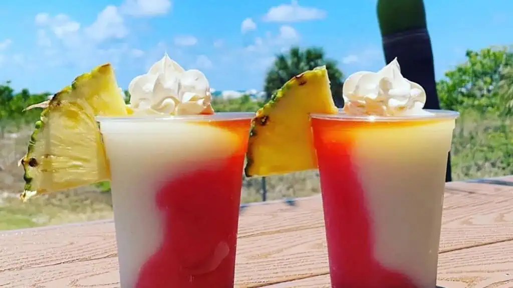 two frozen tropical drinks with pineapple wedges sticking out of the cup on the beach