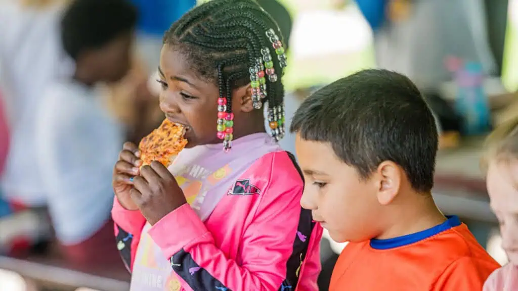 two kids sit at a table and enjoy a meal at a park