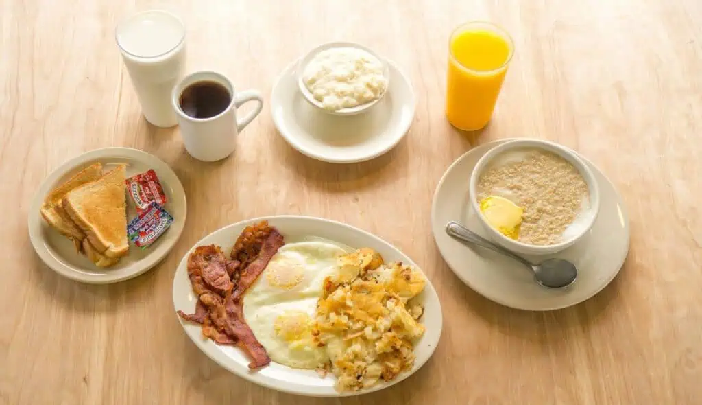 cup of coffee, cup of orange juice, cup of milk, along side a plate of toast and another plate featuring breakfast foods.