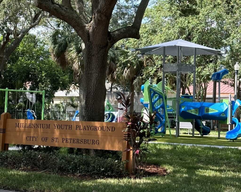 Sign saying Millennium Youth Playground  in front of large shaded playground