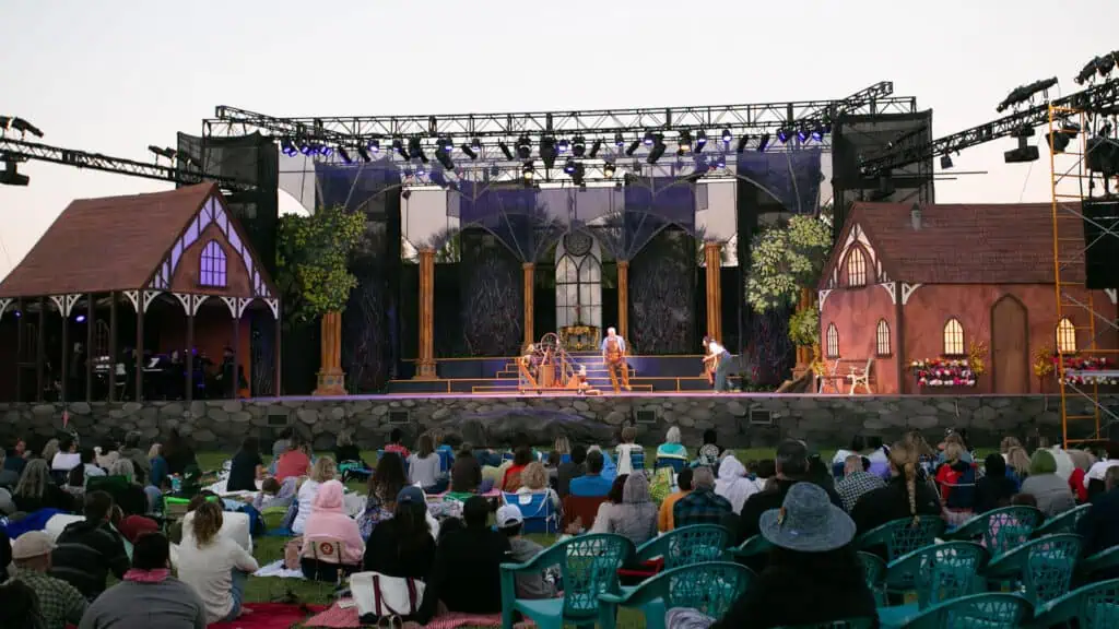 Outdoor at the park, an audience is sitting in front of the stage with performers