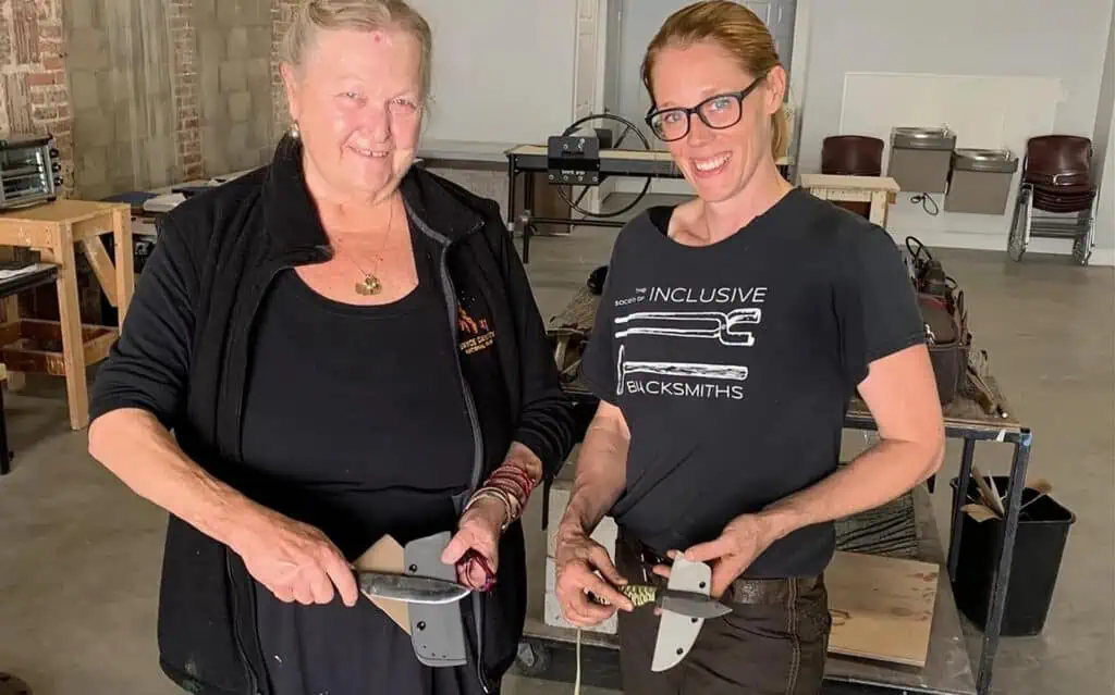 Two people hold up metal work they've created in a workshop 