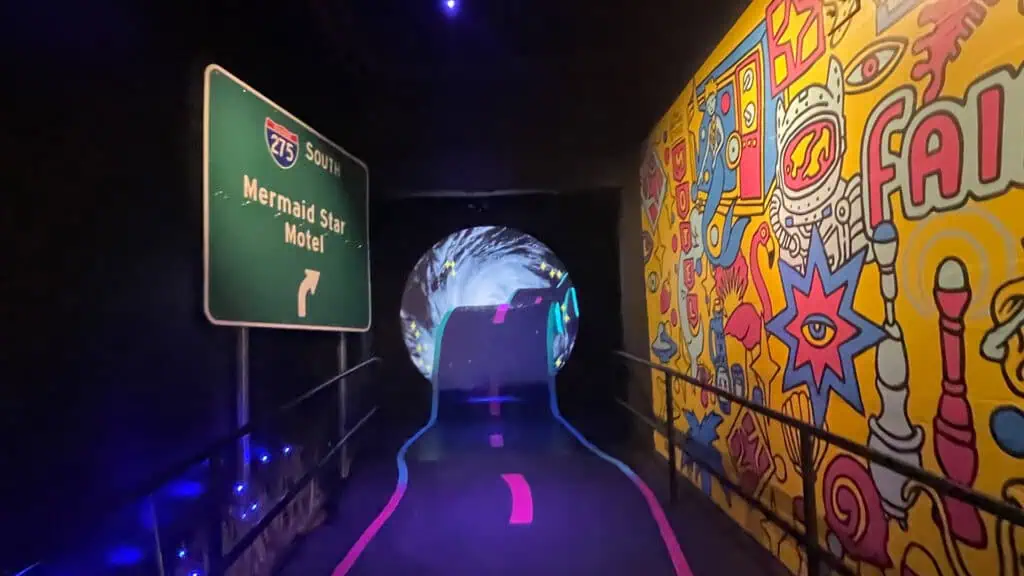 entry way to an arts venue with a yellow mural to the right and a project road way on the floor